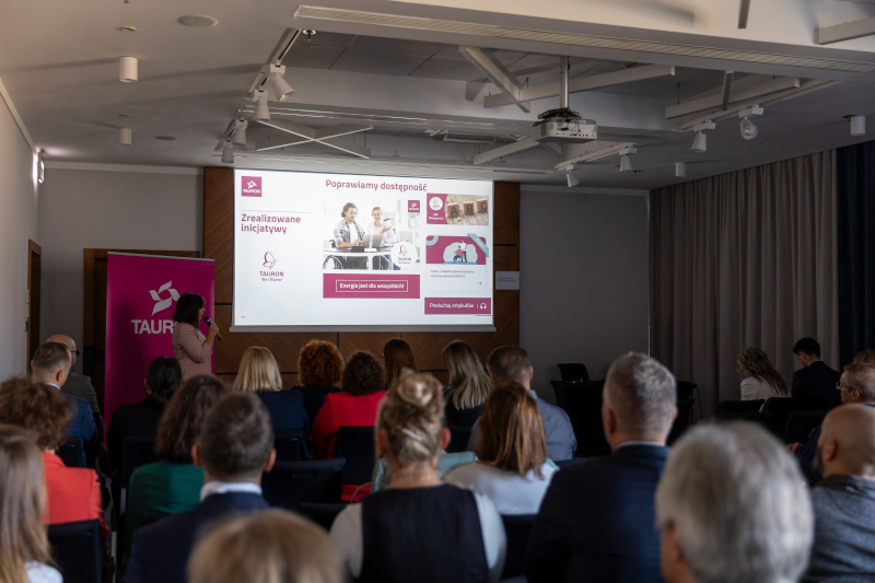 Widok z głębi sali na slajd z informacjami o wdrożonych ułatwieniach na infolinii obsługowej w ramach programu TAURON Bez Barier.  